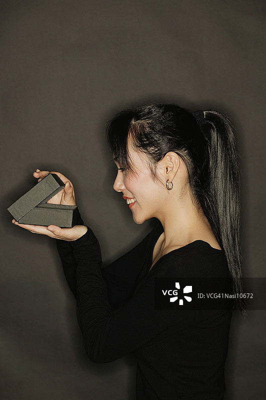 在黑色背景下打开盒子的年轻女人侧影图片素材