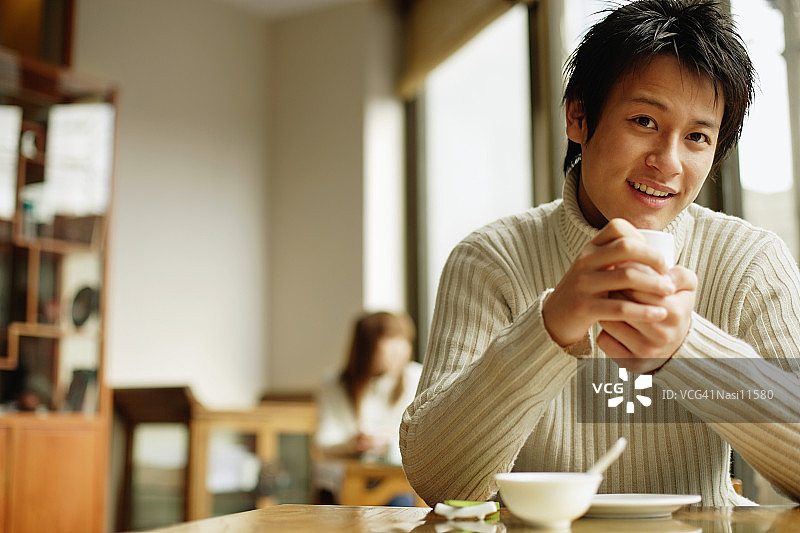年轻人坐在桌旁端着茶杯图片素材