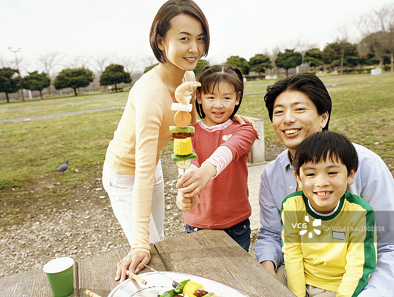 一家人在野餐桌旁，女儿自豪地展示烤肉串图片素材