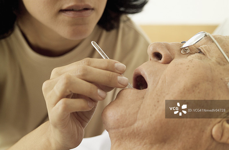 女人将体温计放入老年男人的嘴里，特写图片素材