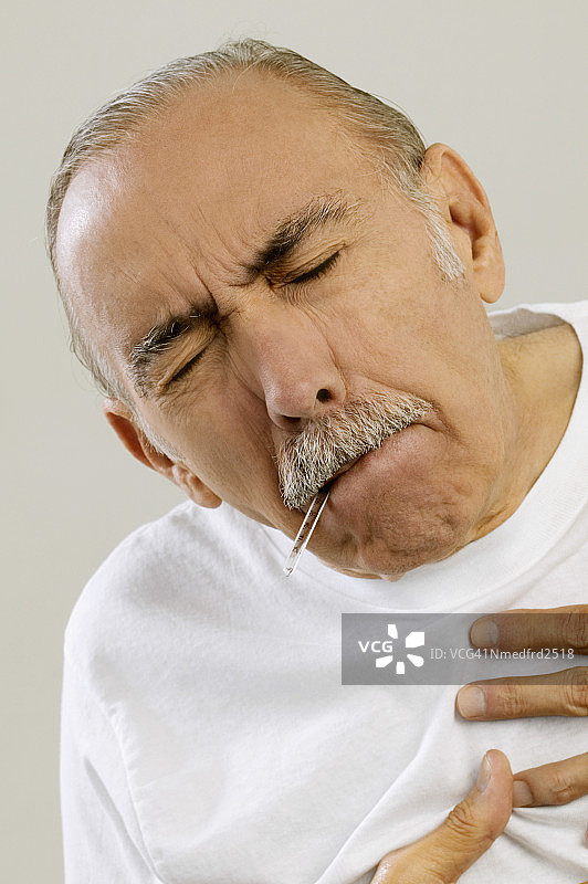 双手放在胸前、嘴里含着体温计的年长男人特写图片素材
