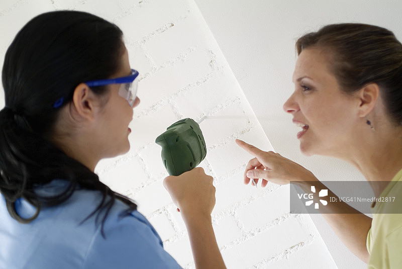 两个女人在砖墙上使用电钻，特写图片素材