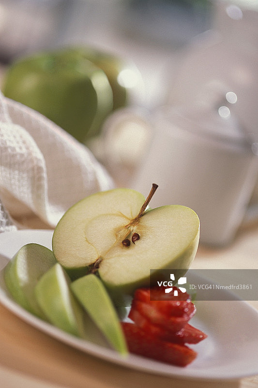 半个苹果与苹果片和草莓片放在盘子里，特写，倾斜拍摄。图片素材