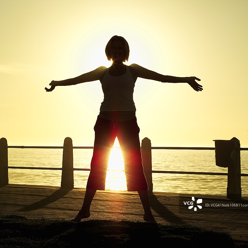 黄昏时分，站在码头上伸展双臂的女人（轮廓）图片素材