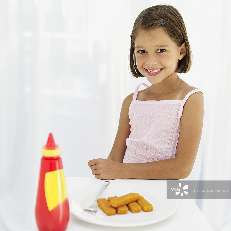 坐在鱼条盘子和番茄酱瓶子旁边的女孩肖像（6-7岁）图片素材