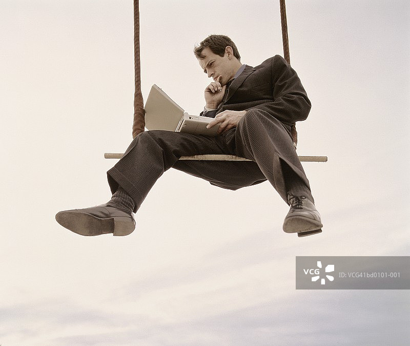 男高管坐在高空秋千上使用笔记本电脑图片素材