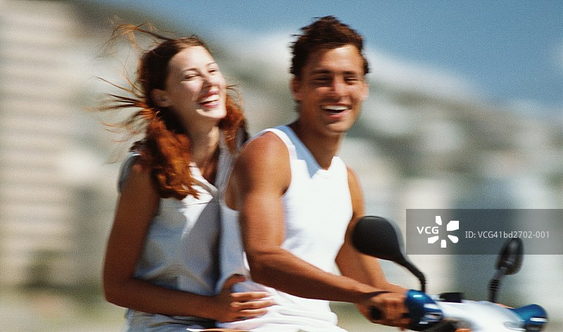 年轻夫妇骑着轻便摩托车，面带微笑（动态模糊）图片素材