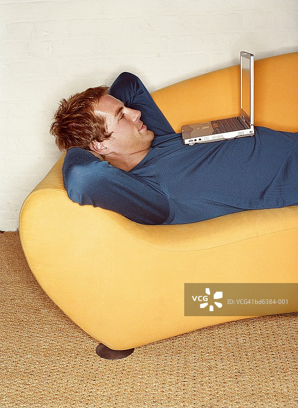 男子躺在沙发上，胸前放着笔记本电脑图片素材