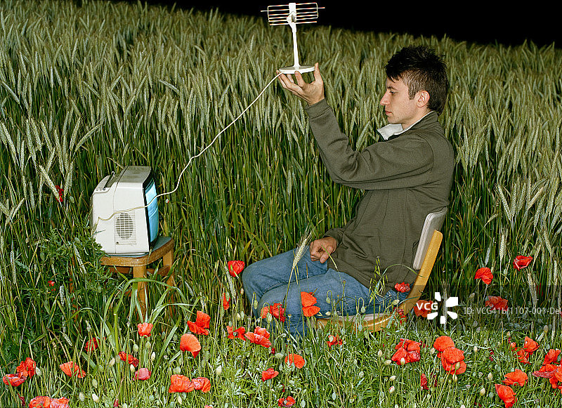 男人在田野里看电视，举着天线，侧面图片素材