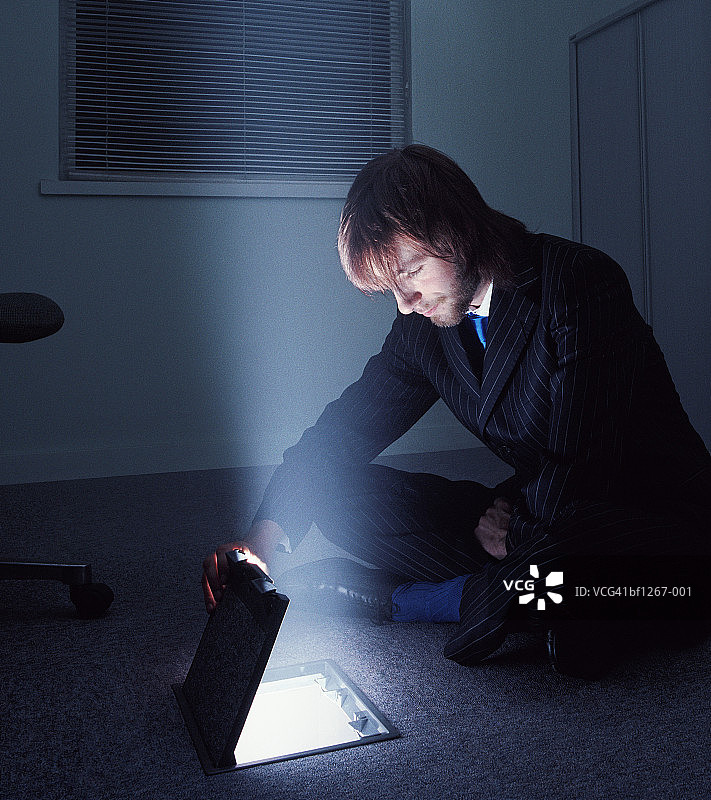 男子盘腿而坐，看着发光的地板盒图片素材