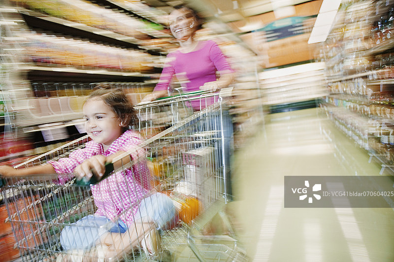 妈妈在超市通道里推着坐在购物车里的女儿（模糊）图片素材