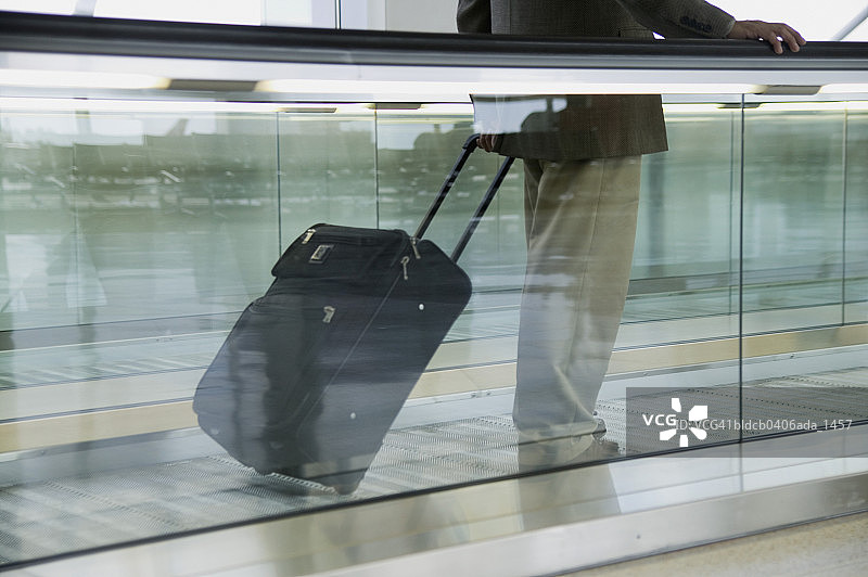 商务人士在机场扶梯上拉着行李的侧面照图片素材