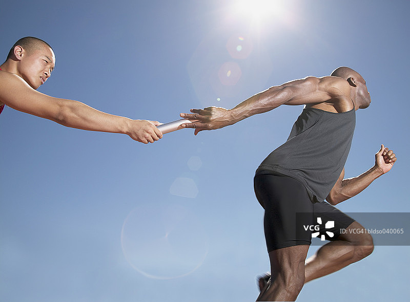 低角度视角：接力赛中一人将接力棒传递给另一人图片素材