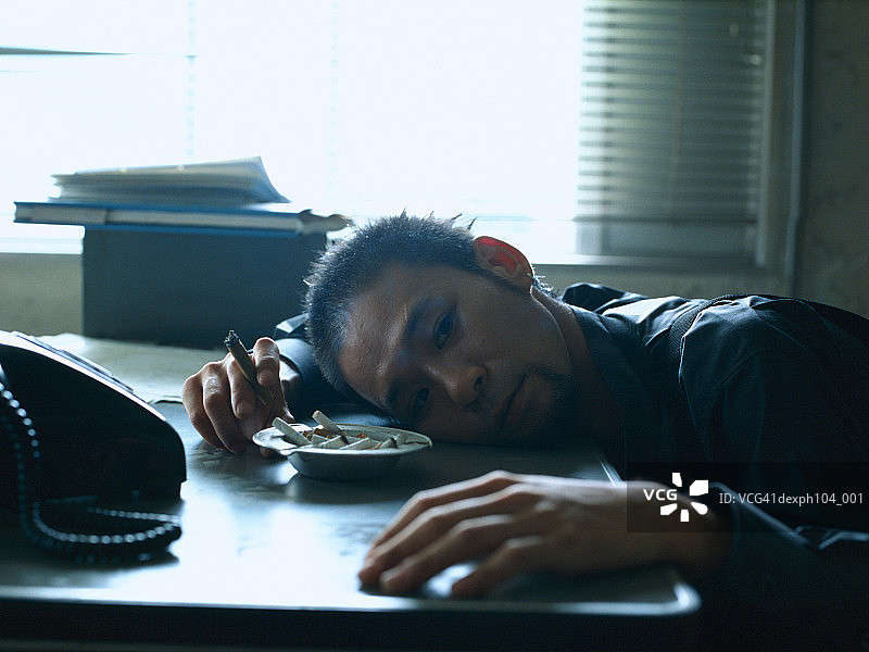 男子头靠在桌子上休息，手 holding cigarette图片素材