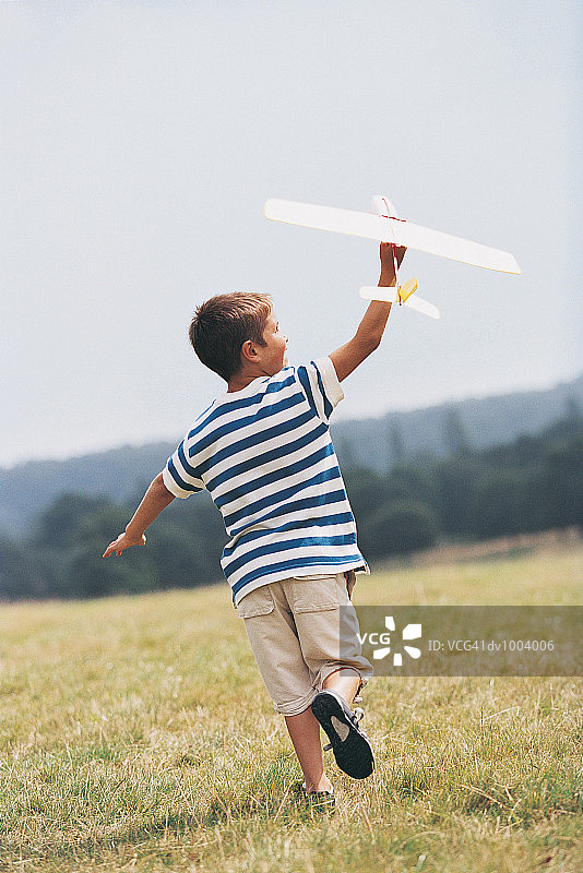 男孩在田野里奔跑，手持玩具飞机的背影图片素材
