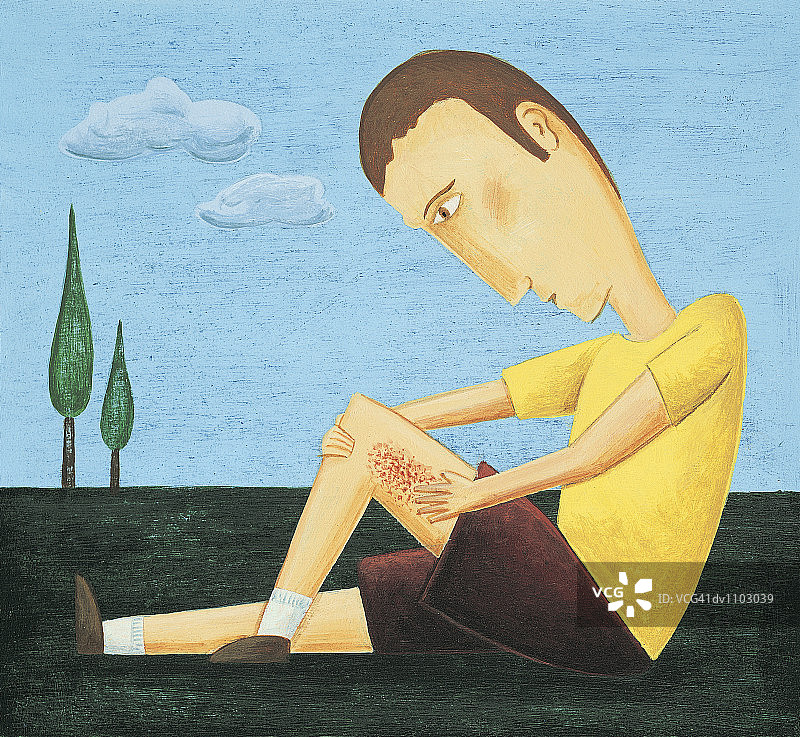 男孩坐在公园里，摸着擦伤的腿图片素材