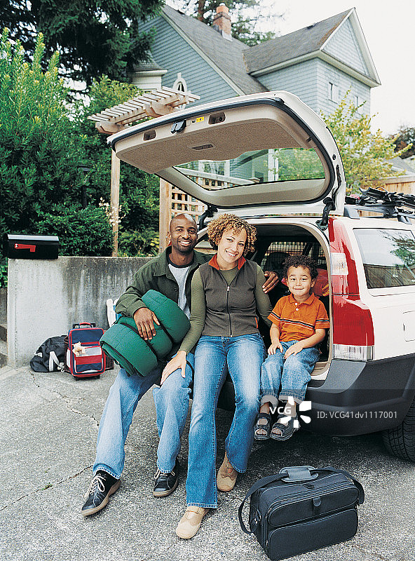 儿子和父母坐在旅行车后备箱里，周围都是行李图片素材