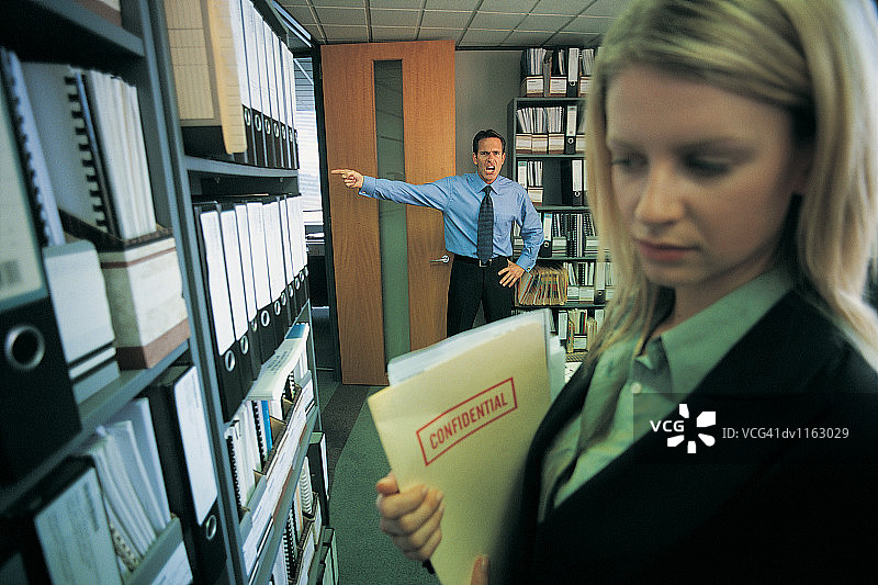 商人发现女商人从办公室的书架上拿走一份机密文件图片素材