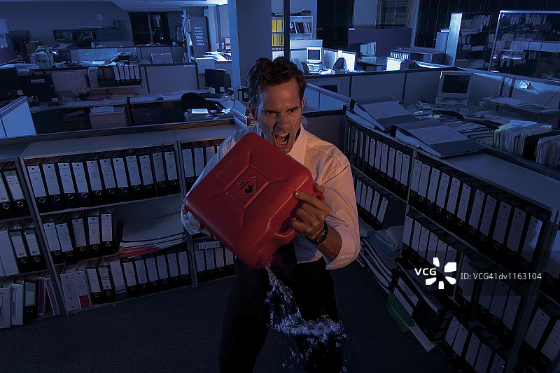 愤怒的商人在开放式办公室里拿着燃料罐倾倒汽油图片素材