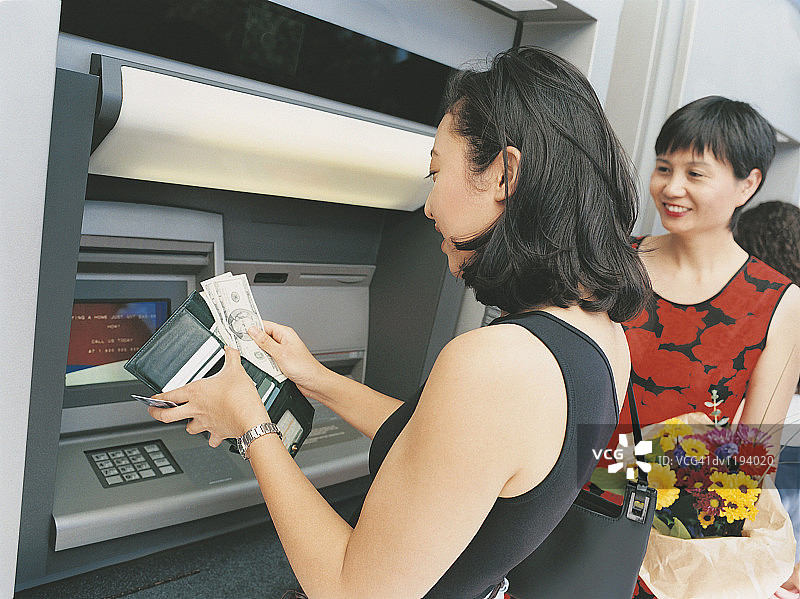 女儿在自动取款机旁取款，将钞票和银行卡放入钱包，母亲手捧鲜花图片素材