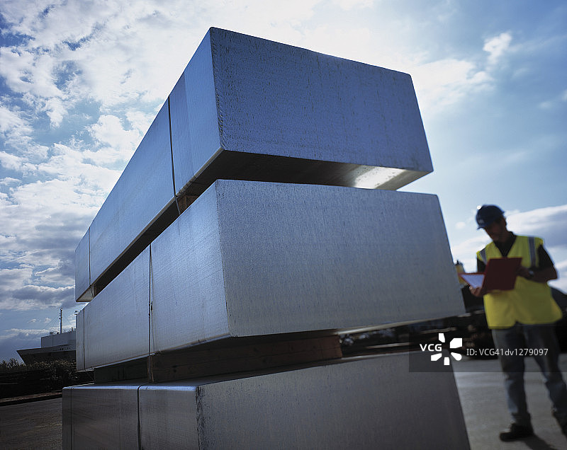 站在三个回收铝块堆旁边的男人，英国亨伯赛德郡伊明厄姆港图片素材