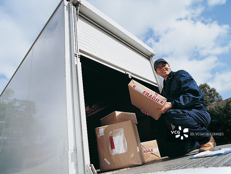 快递员手持包裹蹲在货车液压平台上图片素材
