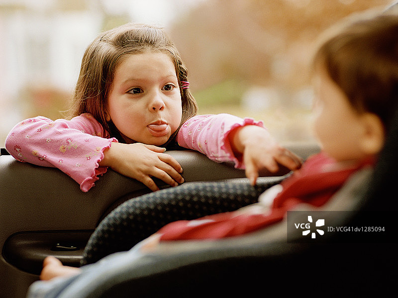 女孩在车窗里对着坐在汽车座椅上的另一个孩子做鬼脸图片素材