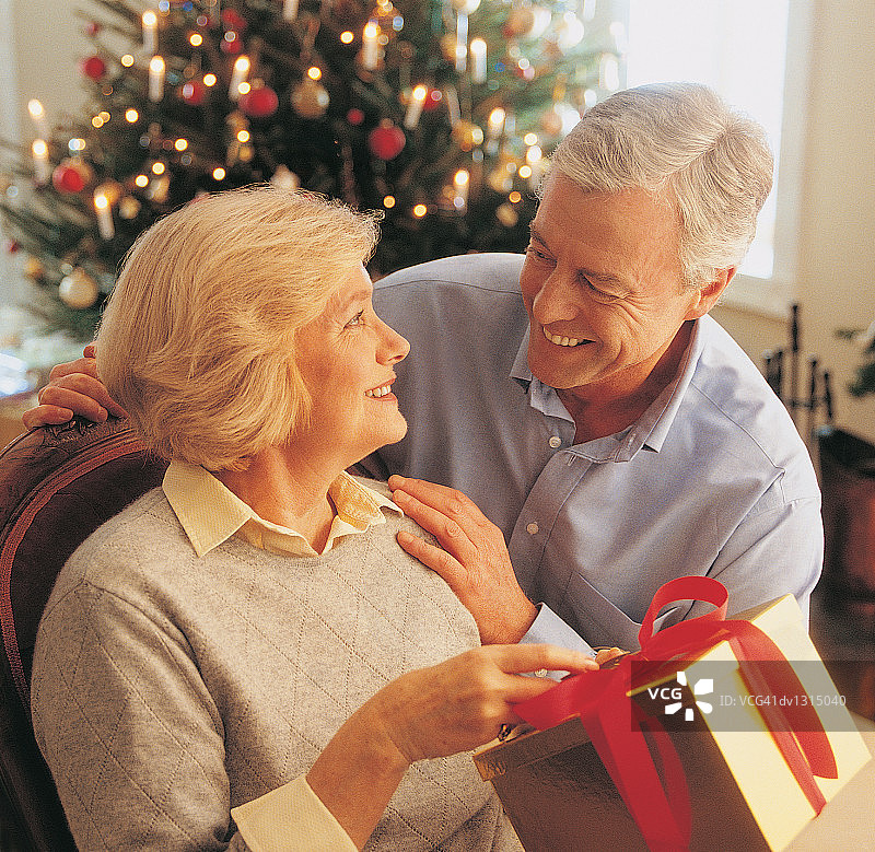 老年夫妇在客厅里庆祝圣诞节，女士拿着礼物图片素材