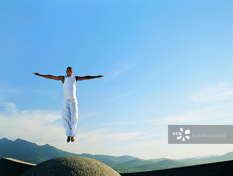 在巨石上空伸开双臂的男人图片素材