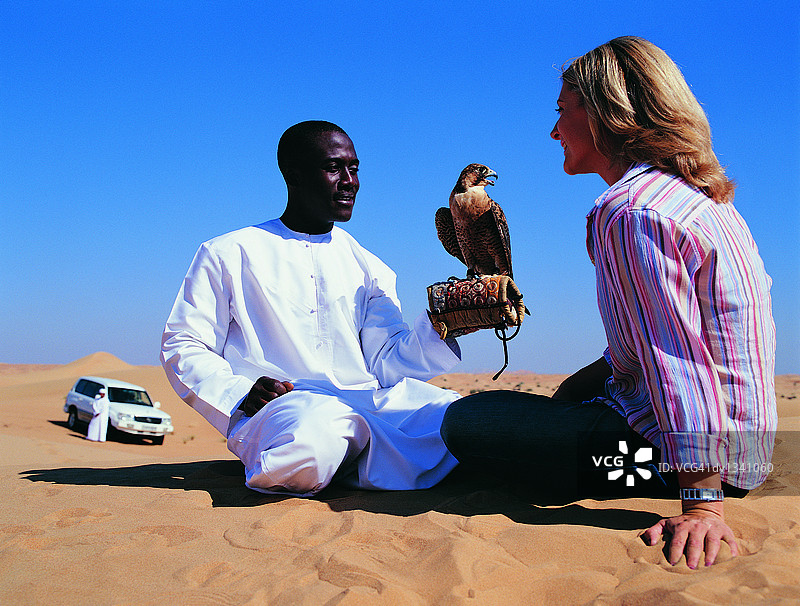 身着中东传统服饰与女子在沙漠中面对面坐着的男人图片素材