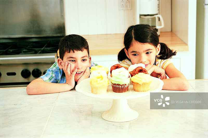 姐妹和兄弟在厨房里凝视着盘中蛋糕图片素材