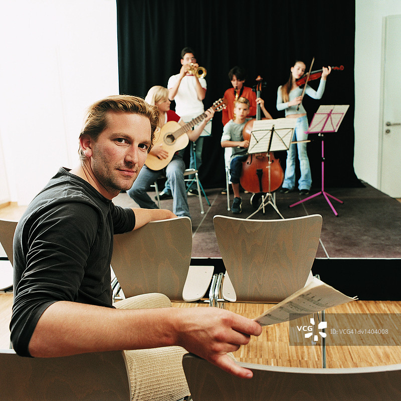 音乐老师坐在椅子上，乐队在舞台上排练图片素材