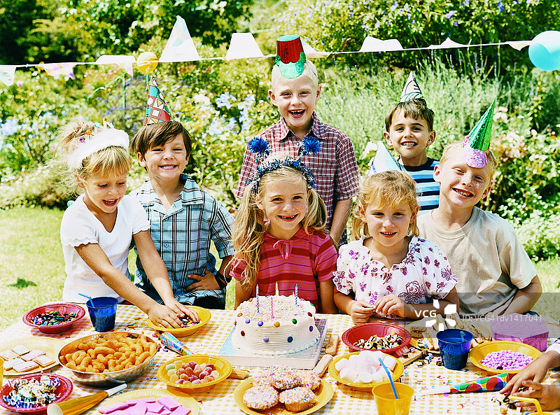 生日聚会上，孩子们站在摆满糖果和生日蛋糕的桌子后面图片素材