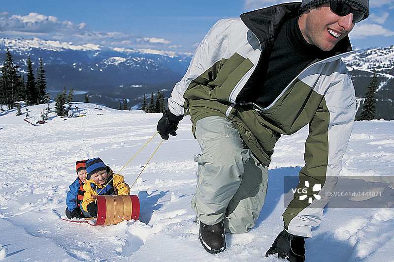 父亲拉着两个儿子在雪山上乘坐雪橇图片素材
