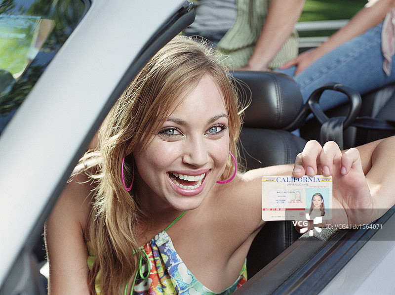 少女坐在敞篷车的驾驶座上，拿着身份证图片素材