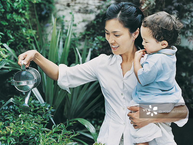 母亲带着儿子在花园里用水壶浇花图片素材