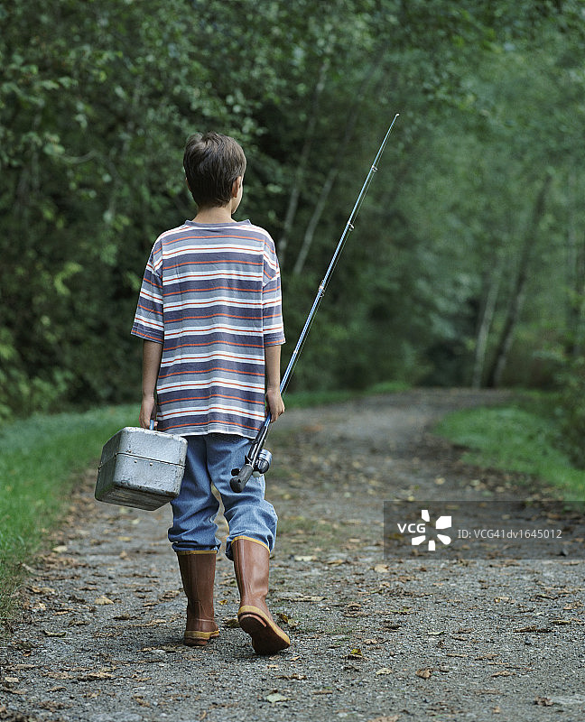 拿着钓鱼竿和工具箱走在森林小路上的小男孩背影图片素材