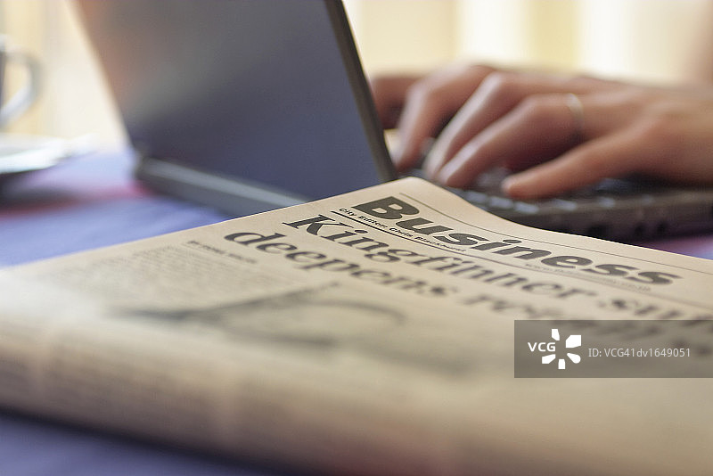 桌子上的商业报纸，背景中有人使用笔记本电脑图片素材