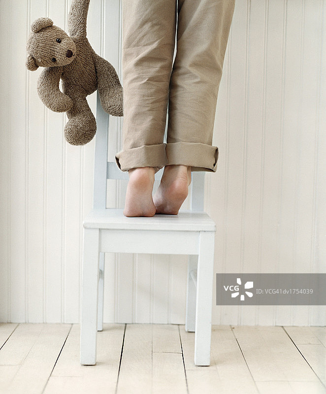 儿童站在椅子上，泰迪熊在一旁的后视图图片素材