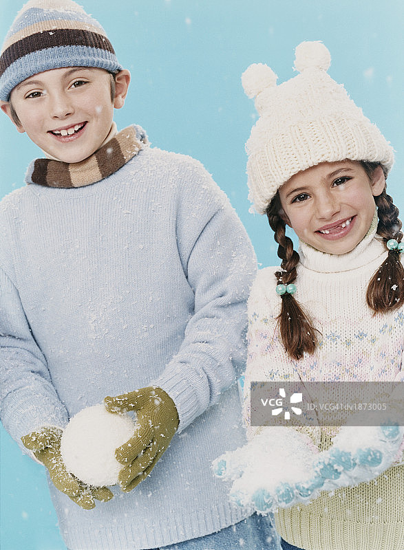 身穿冬装、手拿雪球的年轻男孩和女孩的影棚人像照图片素材