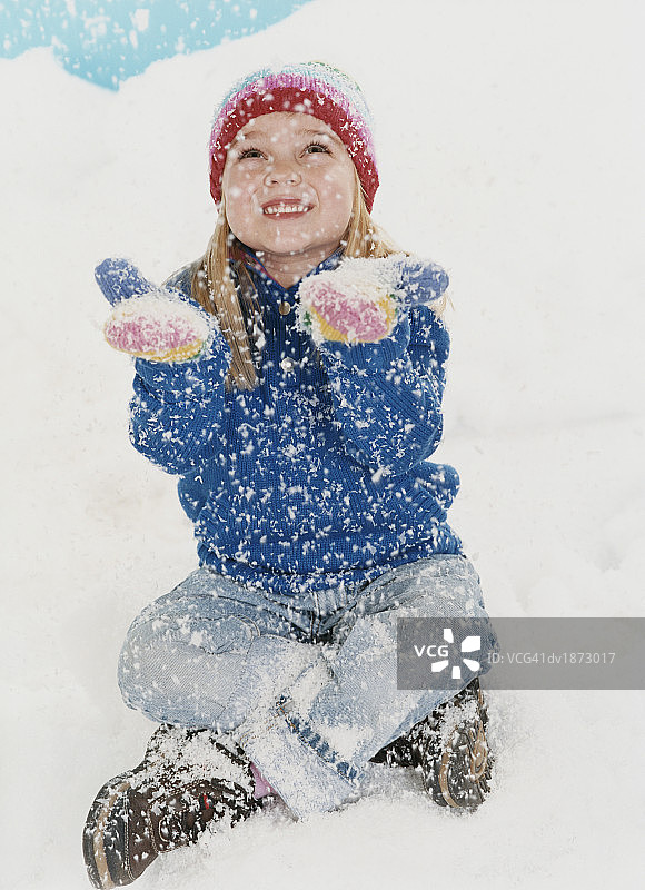 身穿冬装的年轻女孩坐在雪地里，抬头用连指手套接雪花图片素材