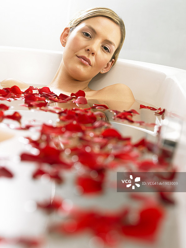 微笑女人在充满红色玫瑰花瓣的浴缸里放松图片素材