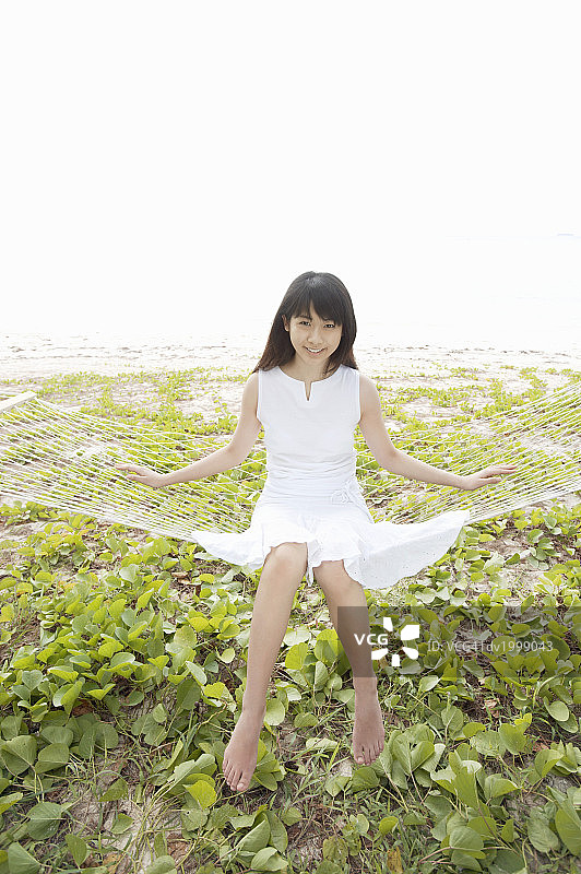 穿着夏装坐在吊床上的年轻女人肖像图片素材