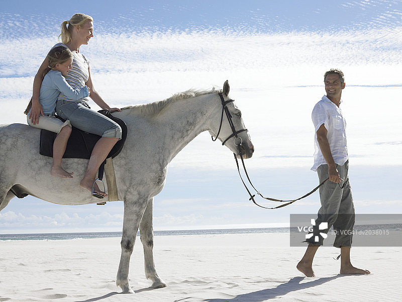 男人和妻子女儿在海滩上牵马图片素材