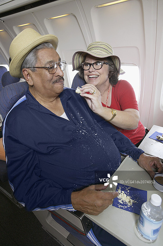 在客机上，年长女性给满身面包屑的男人喂饼干图片素材
