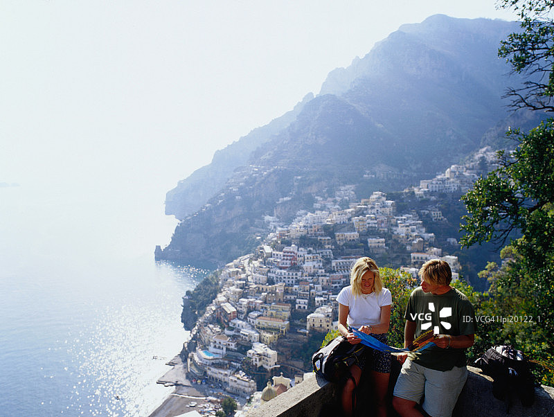 情侣在意大利波西塔诺小镇的瞭望台上阅读旅游指南图片素材