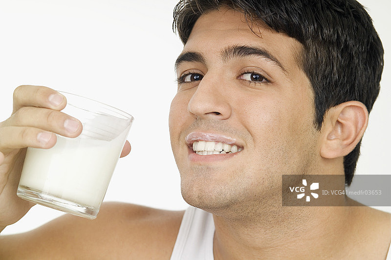 面带微笑的年轻男子，嘴唇沾着牛奶，拿着一杯牛奶特写图片素材