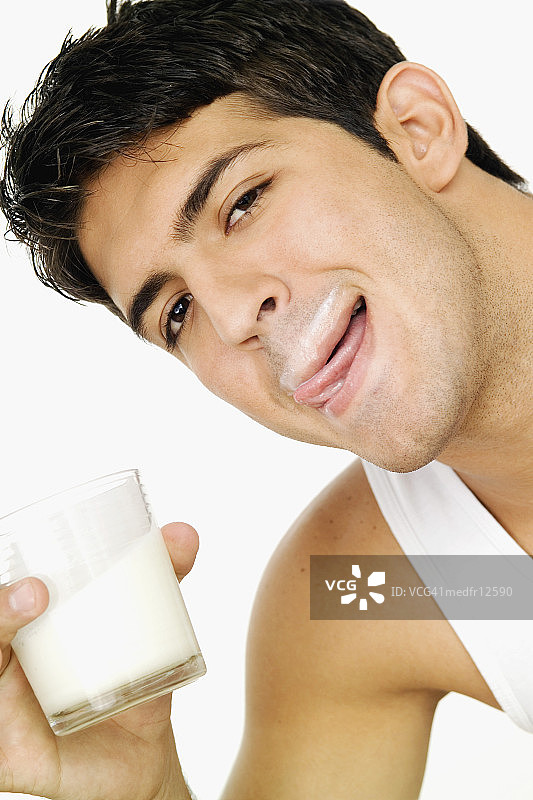 嘴唇沾着牛奶的青年男人，舔着嘴唇，拿着一杯牛奶的特写镜头图片素材
