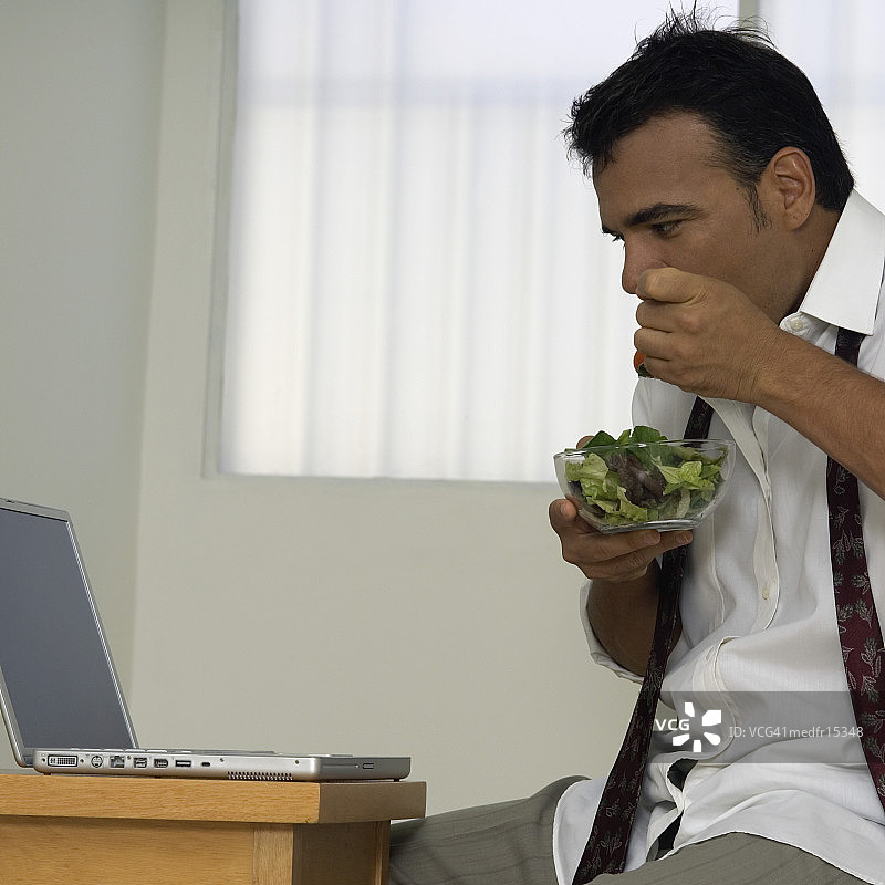 商务人士吃沙拉并看笔记本电脑图片素材