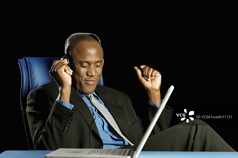 商人坐在办公室戴着耳机听笔记本电脑里的音乐图片素材